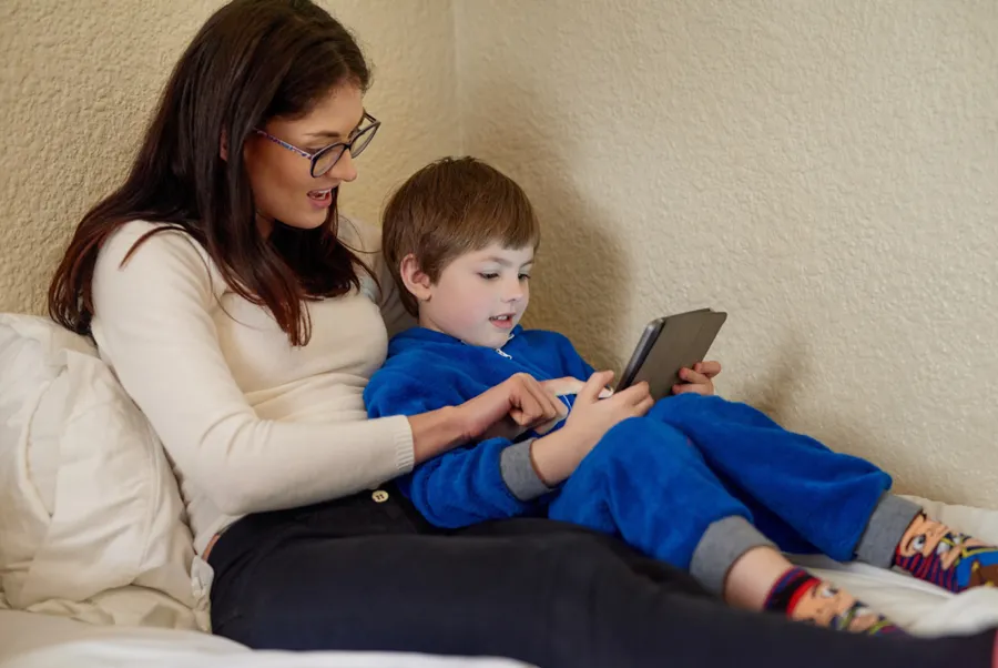 Mãe e filho usando a prancha no celular, sentados na cama